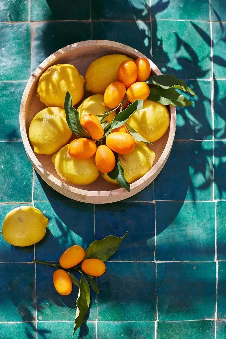 Bol en bois avec citrons jaunes et kumquats sur tomettes vertes